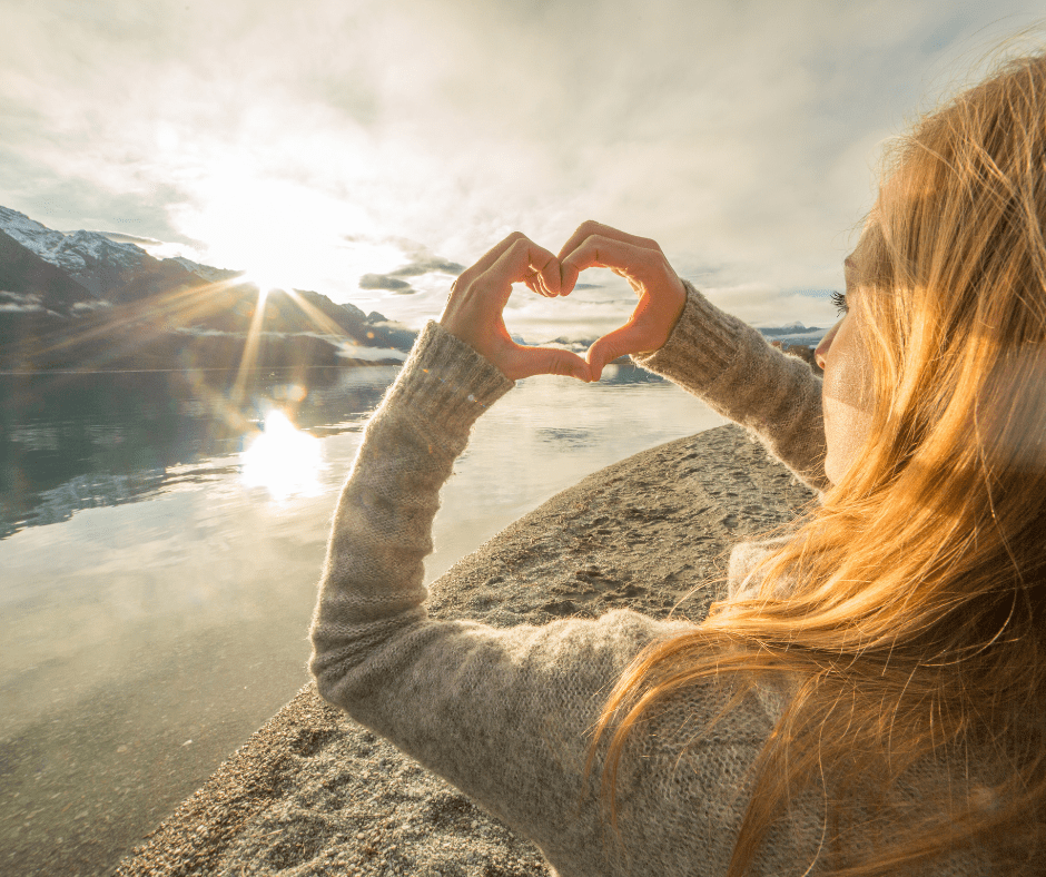Image of lady making a heart with her hand on beach